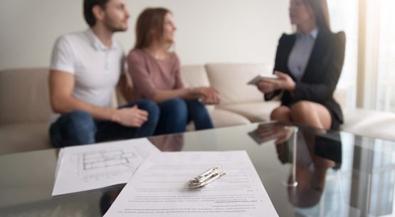 Couple meeting with realtor, focus on rental agreement and keys