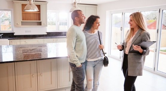 female-real-estate-agent-showing-couple-interested-in-buying-around-house